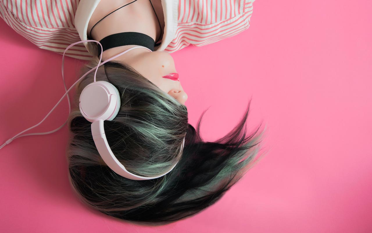 Una mujer con auriculares vestida de rosa sobre un fondo rosa.