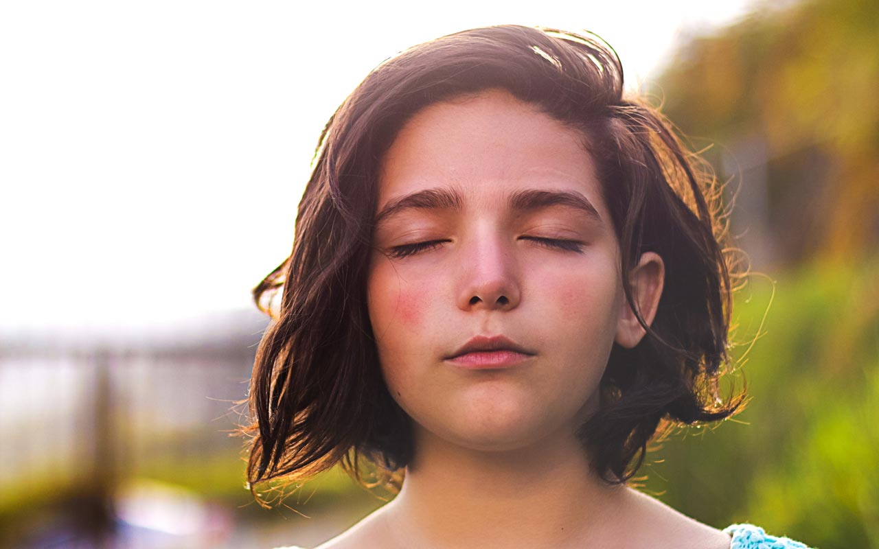 Une jeune femme aux yeux fermés sur un fond extérieur flou.